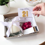 AyeDoGifts 21st birthday hamper with gold number balloons, vanilla candle, silver bracelet, chocolates, and matches.
