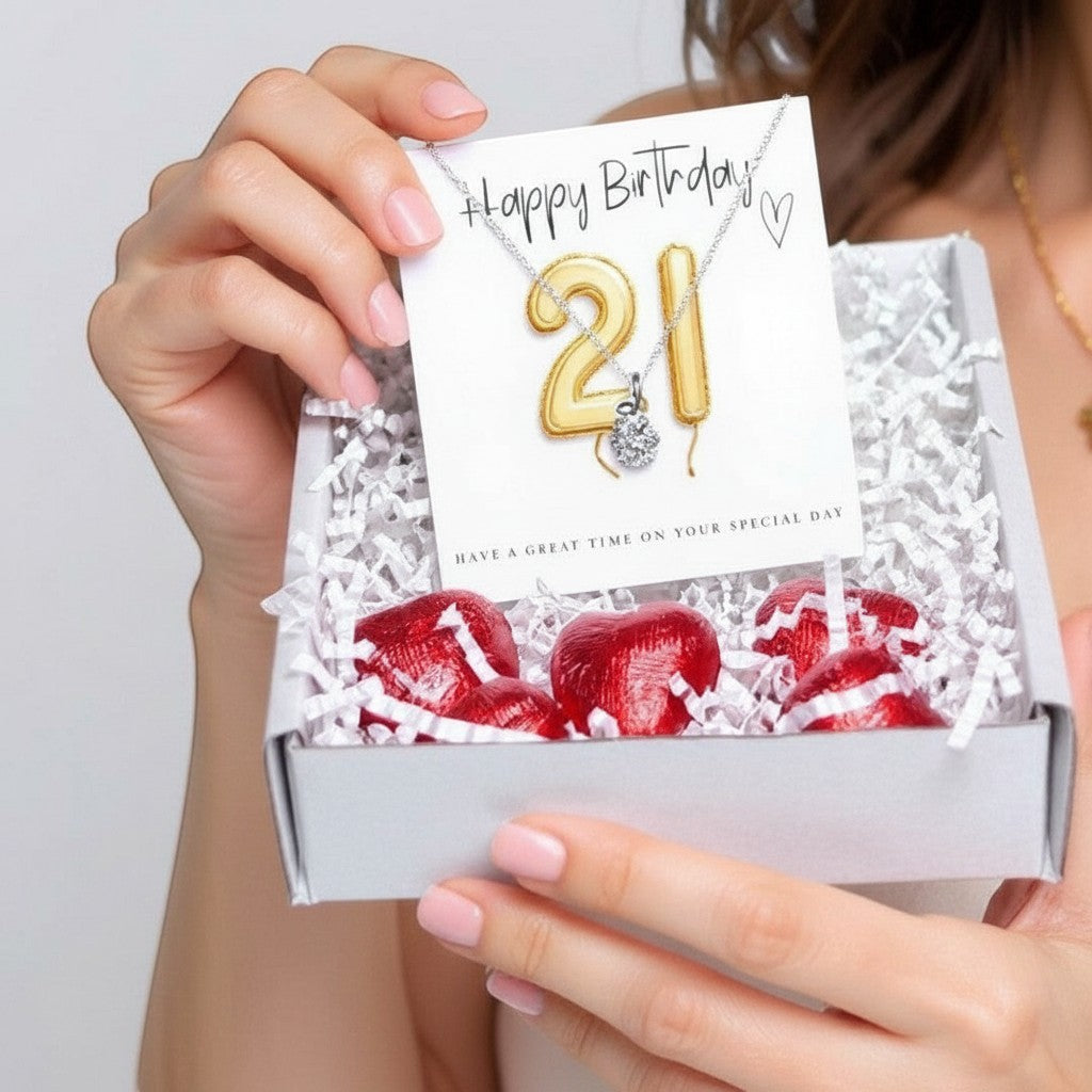 AyeDoGifts 21st birthday gift hamper with silver necklace, cubic zirconia charm, gold balloons card, and chocolate hearts.