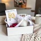 AyeDoGifts 50th birthday gift hamper with gold balloon card, cubic zirconia stud earrings, vanilla candle, matches, and chocolate hearts.